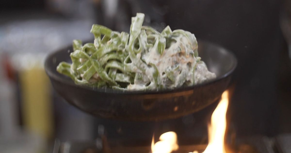 Creamy pasta tossed in a pan over the burner